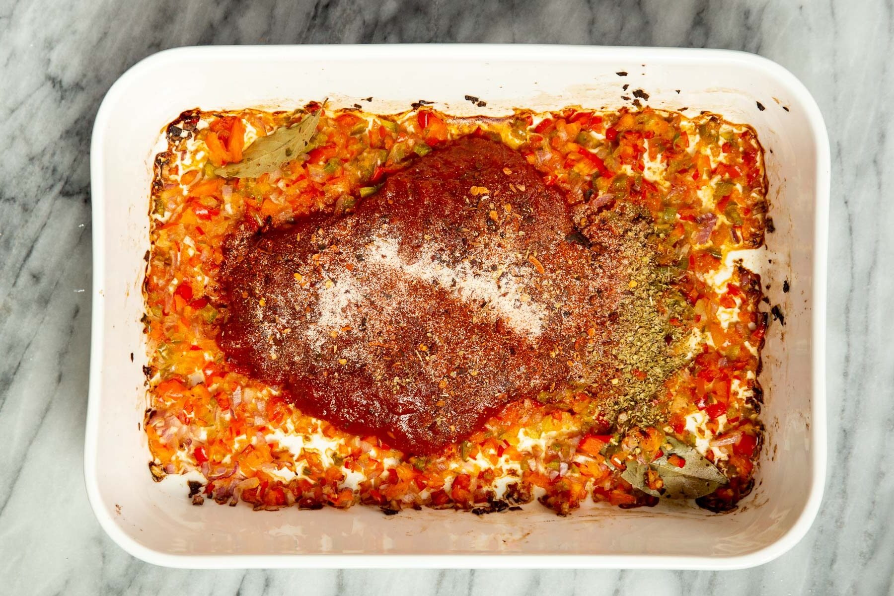 tomato paste being added into a casserole dish with minced sauteed bell pepper onion and spices