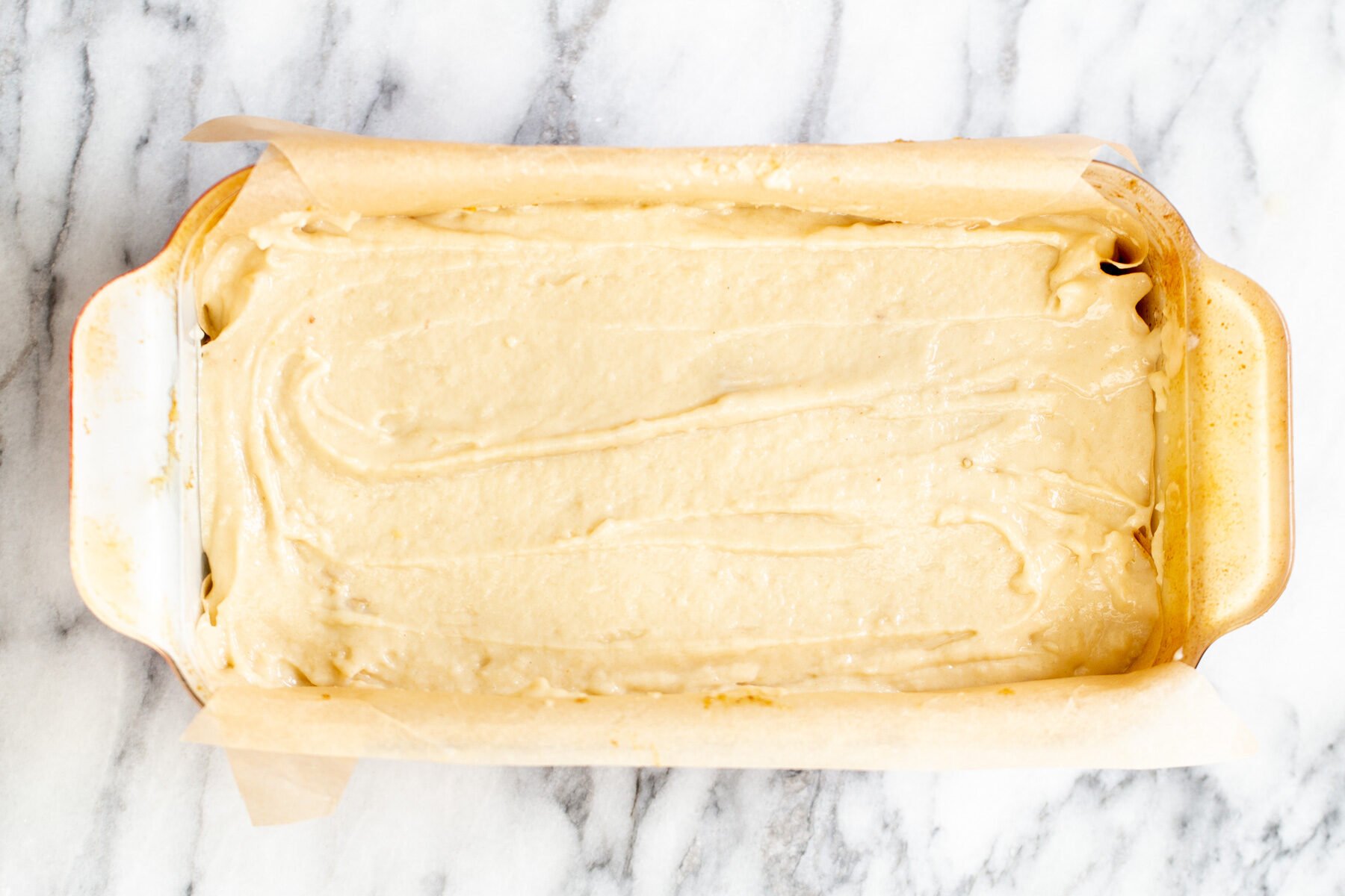 a loaf pan with cake batter on a marble counter.