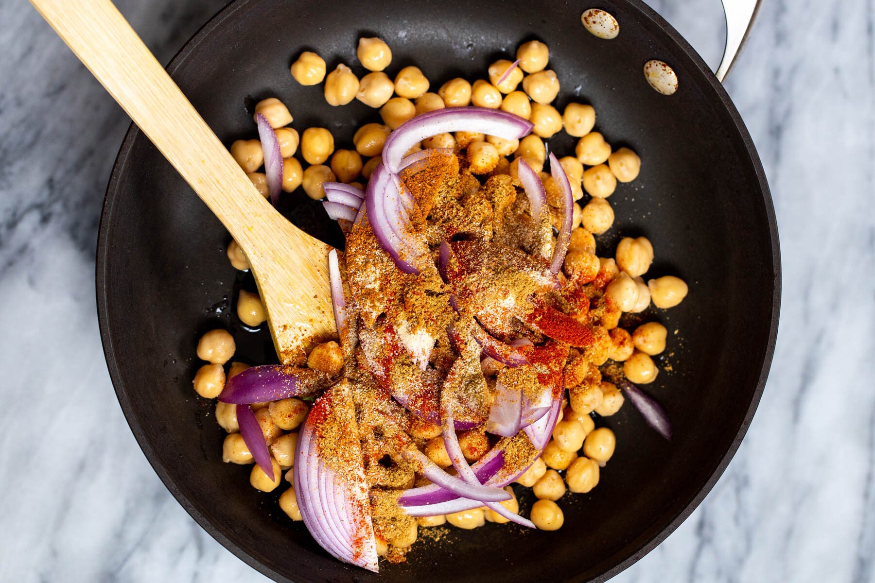canned chickpeas, sliced red onion and Ethiopian spices in a black pan