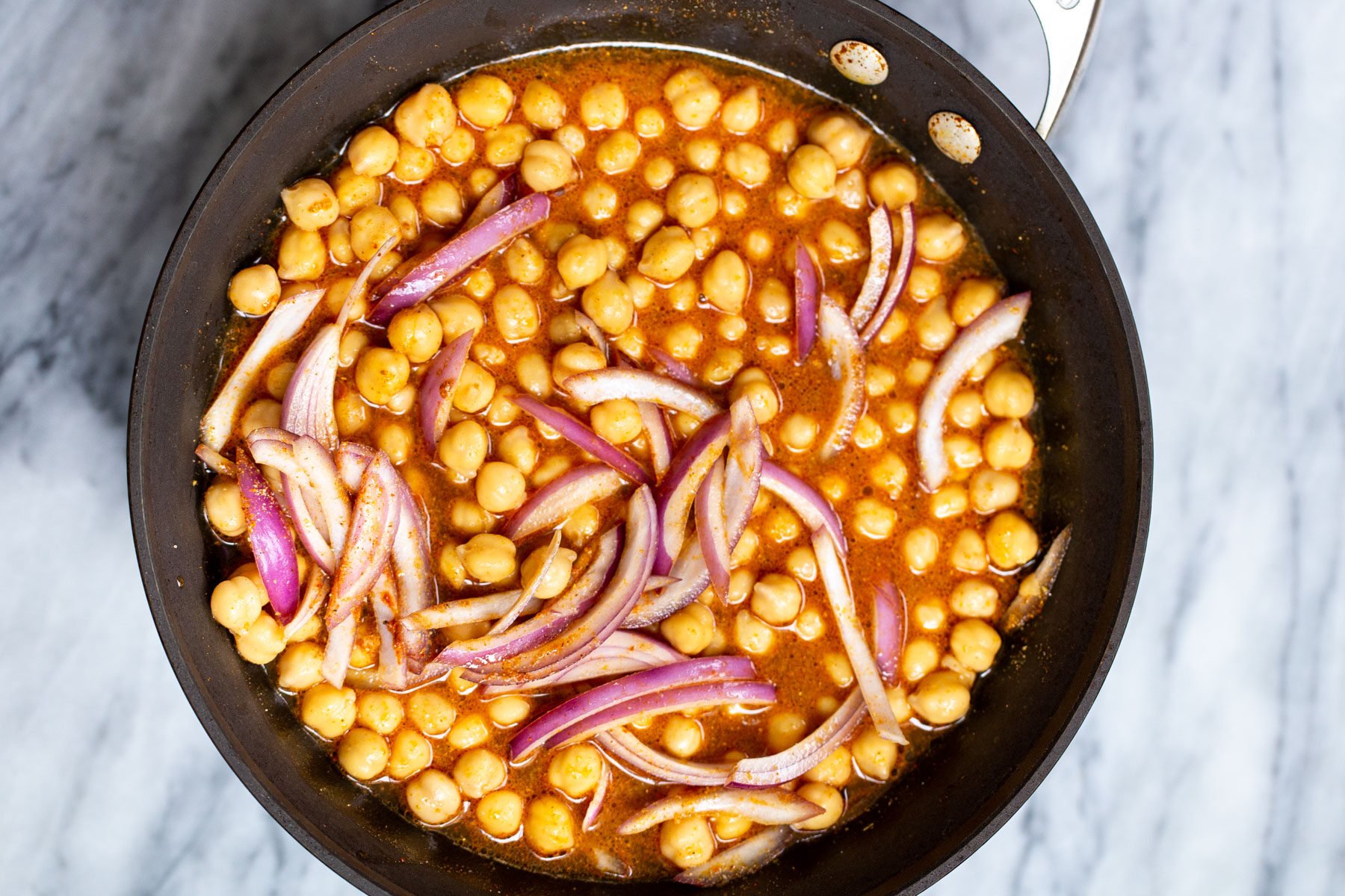chickpeas and sliced red onions with Ethiopian gravy in a black sauteeing pan