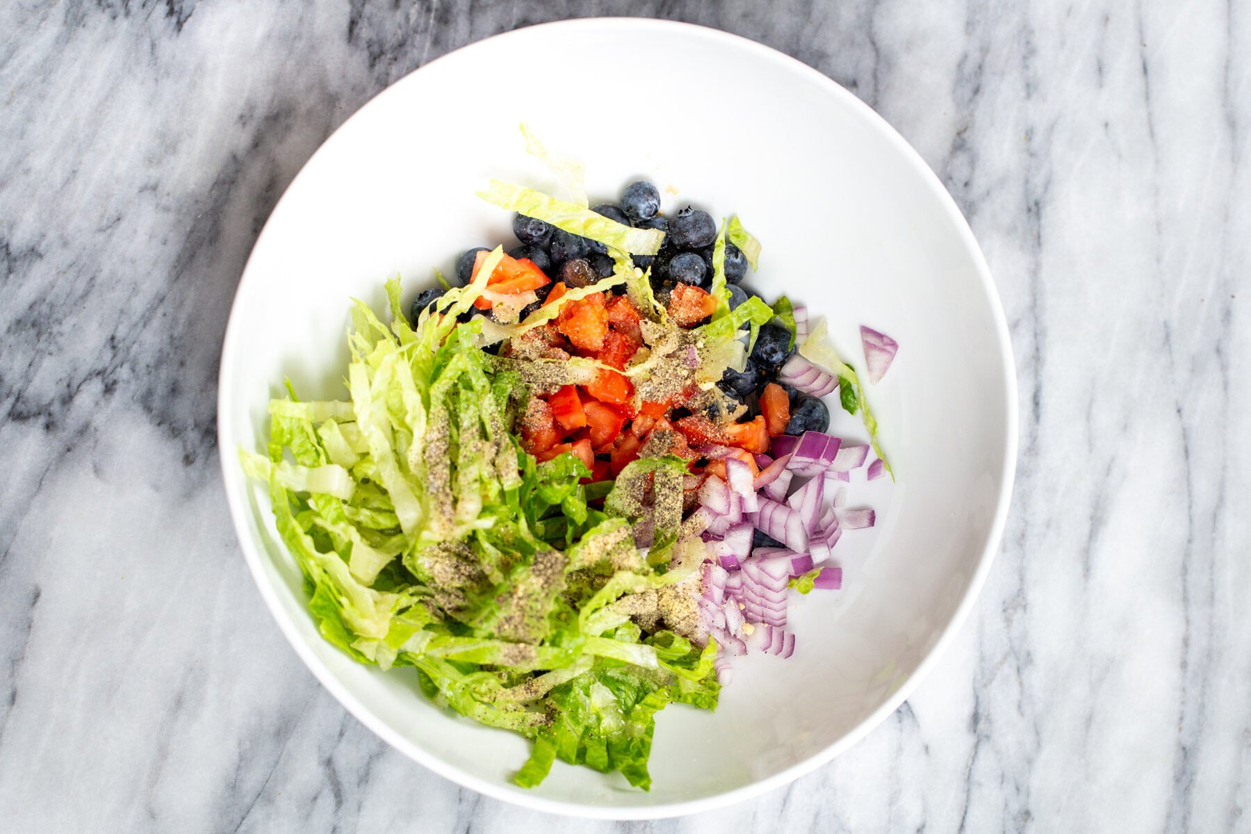 lettuce, blueberries, tomatoes and onion in a white bowl