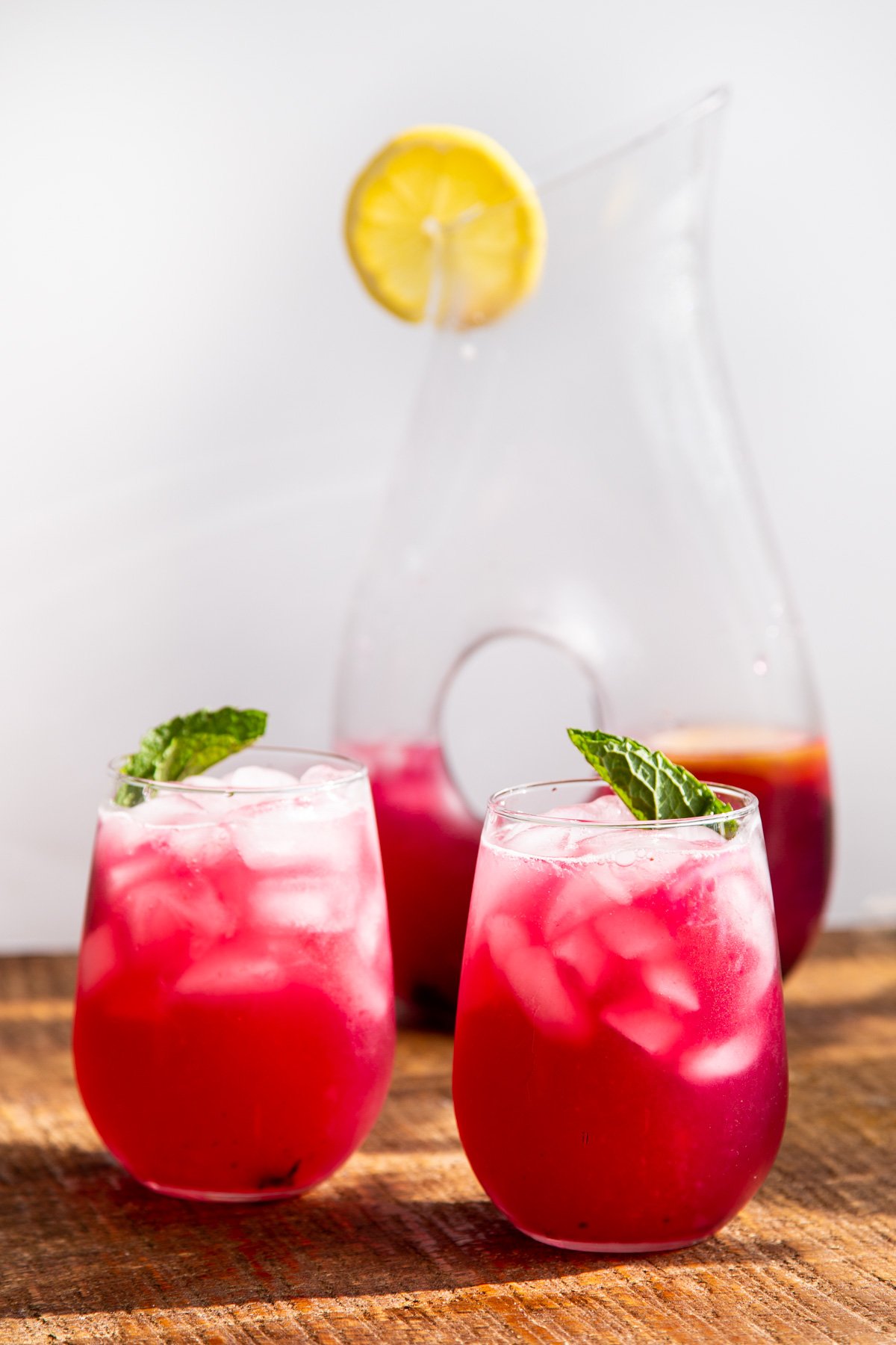 two glasses with homemade fresh blueberry lemonade with a jar of lemonade in the background