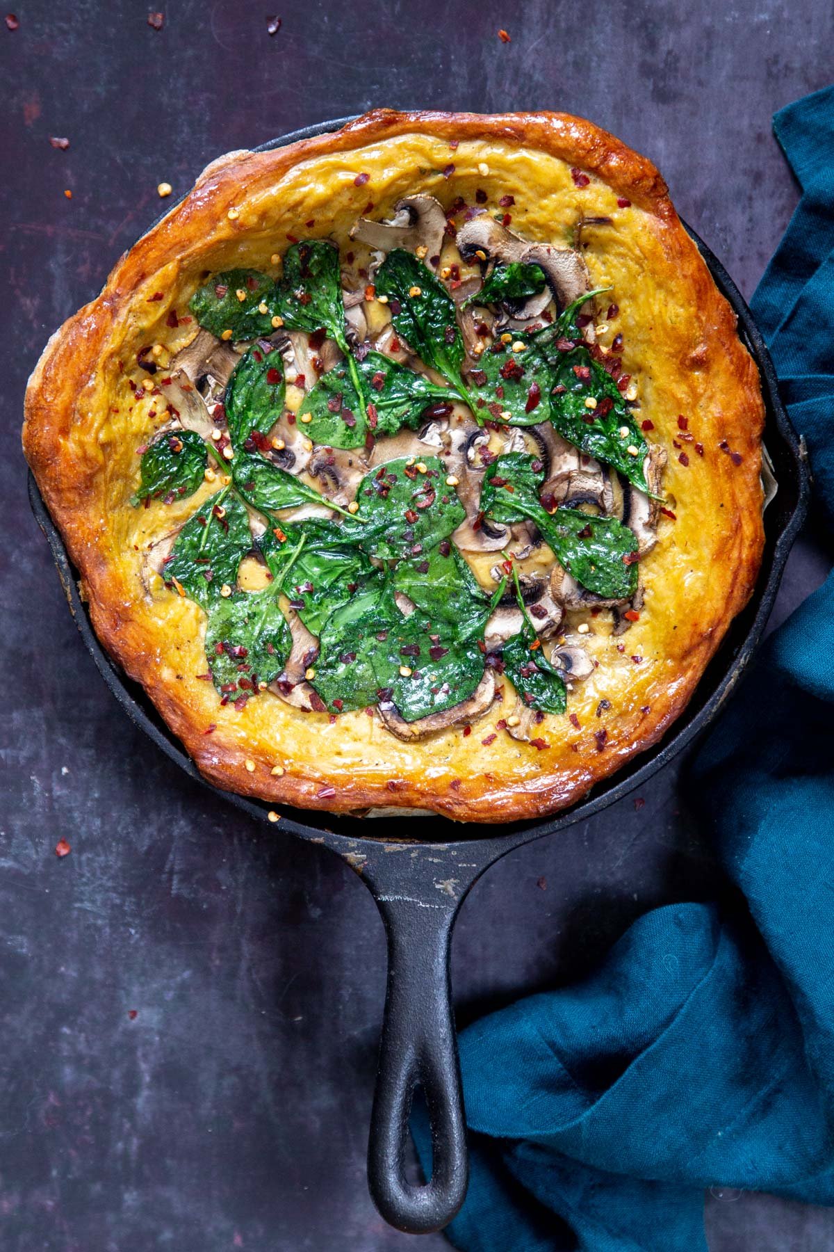 vegan deep dish pizza in a black skillet topped with spinach and mushrooms