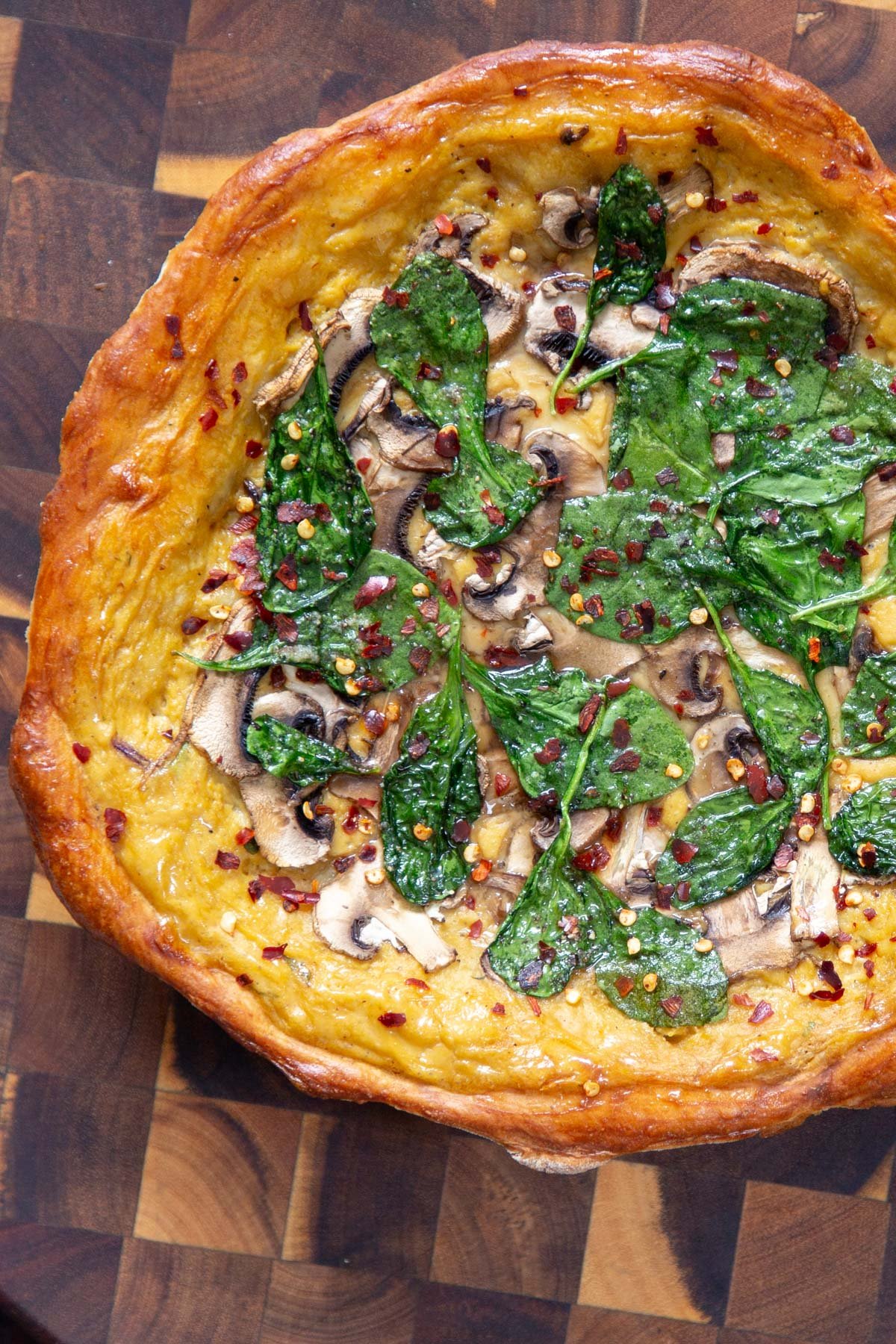 vegan deep dish pretzel crust pizza topped with cheese sauce, mushrooms and spinach on a wooden board