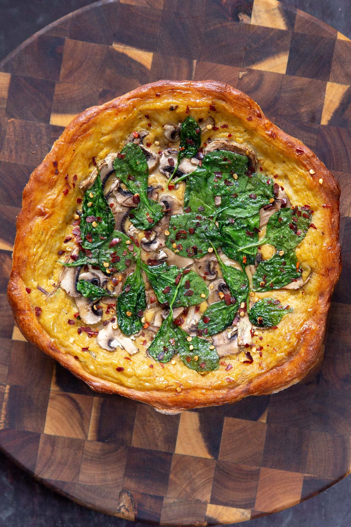 vegan pretzel crust pizza with cheese sauce, spinach and mushroom as well as pepper flakes cooling on a wooden board