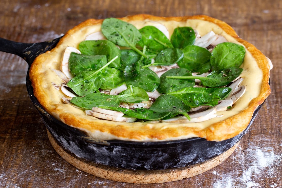 vegan pretzel crust pizza in a black skillet topped with mushrooms and spinach
