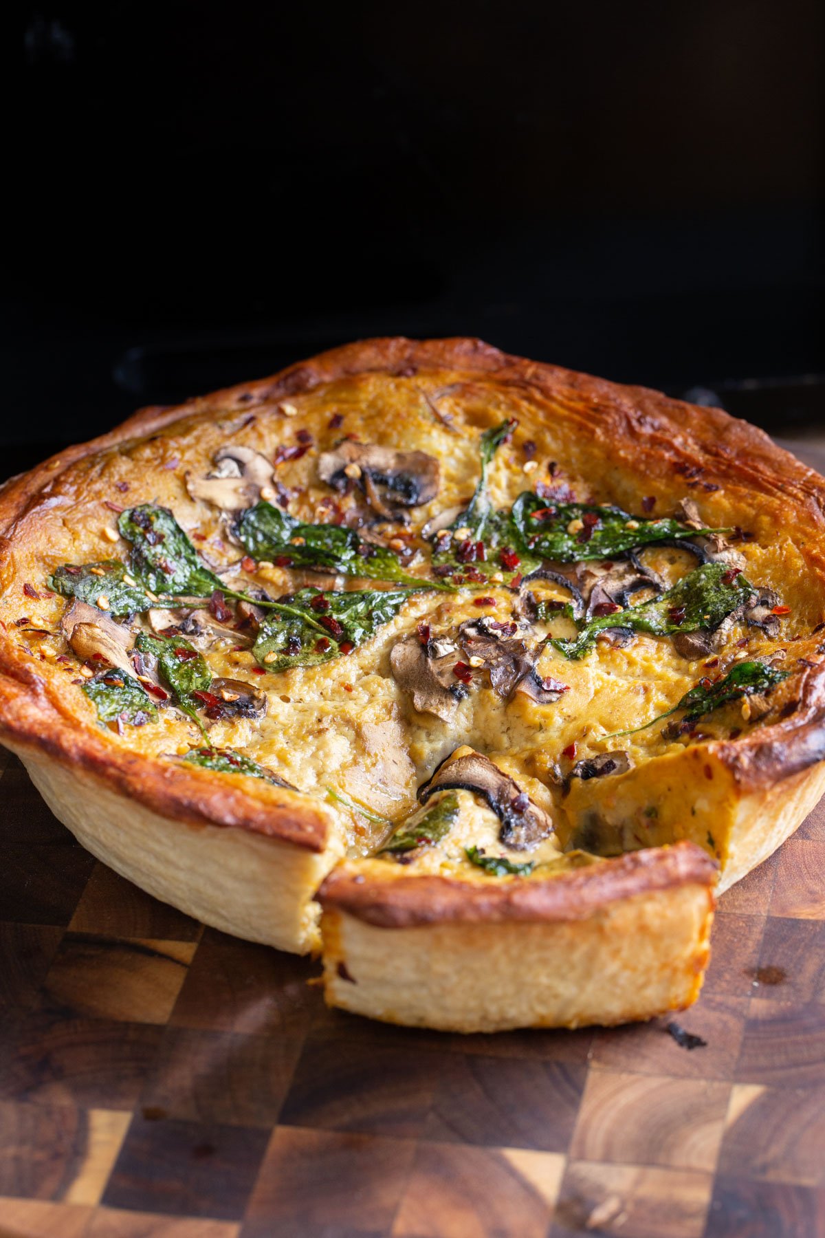 vegan deep dish pretzel crust pizza with cheese spinach and mushroom filling on a wooden board