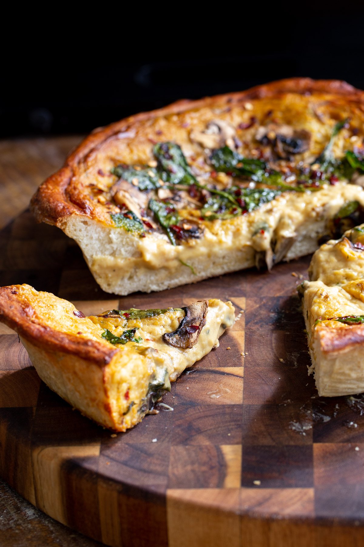 vegan deep dish pizza on a wooden board with one slice being cut
