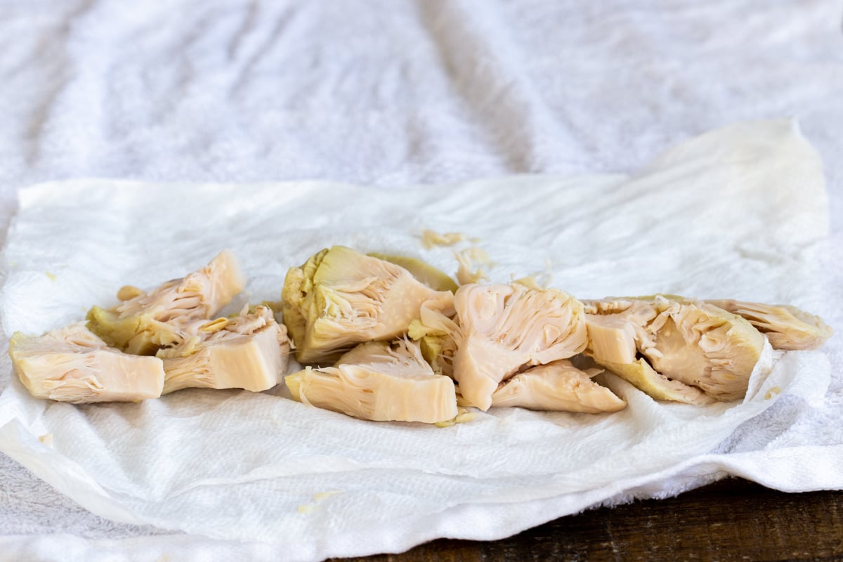 canned sliced of jackfruit being blotted dry on a sheet of paper towels