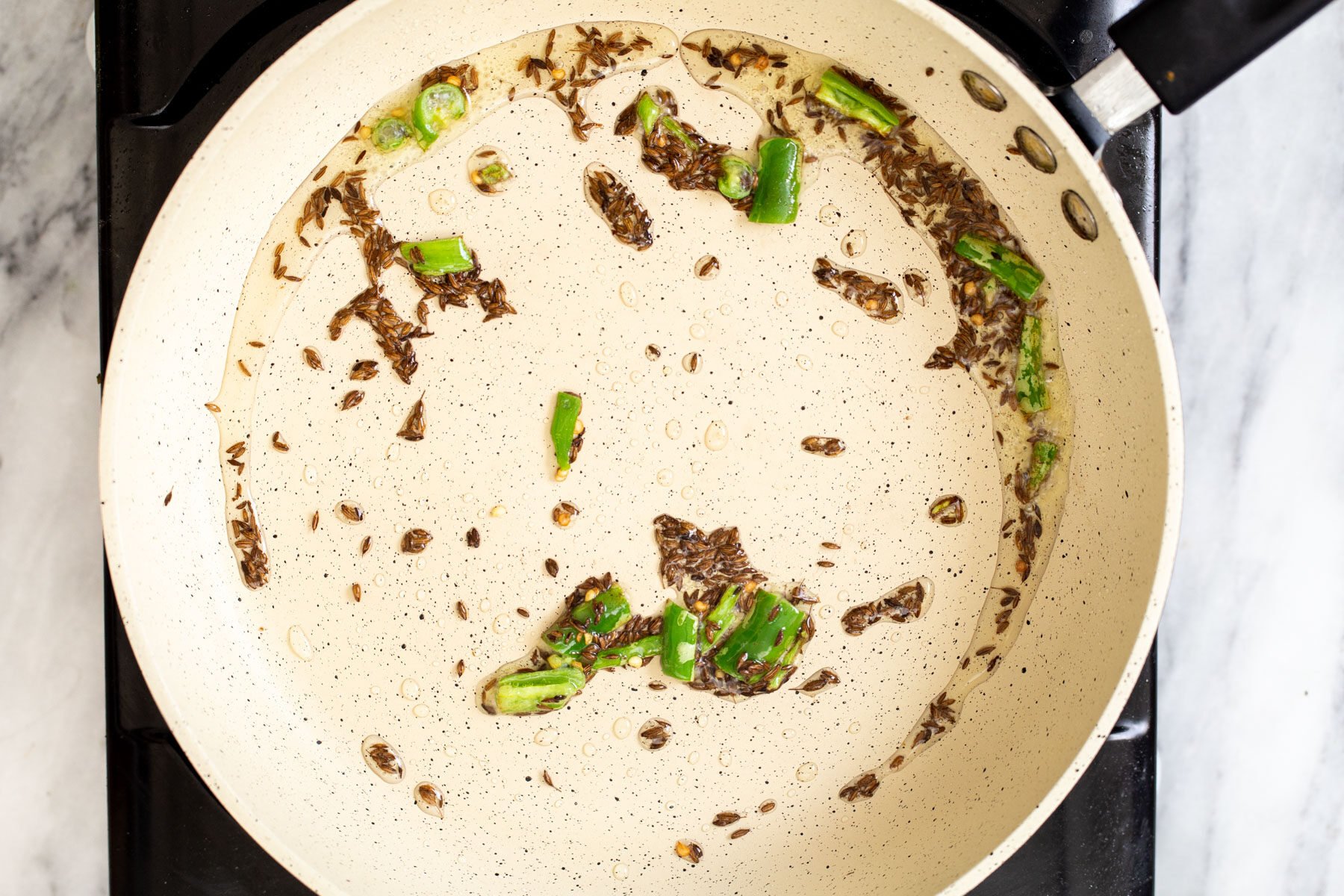 green chili and cumin seeds frying in a pan