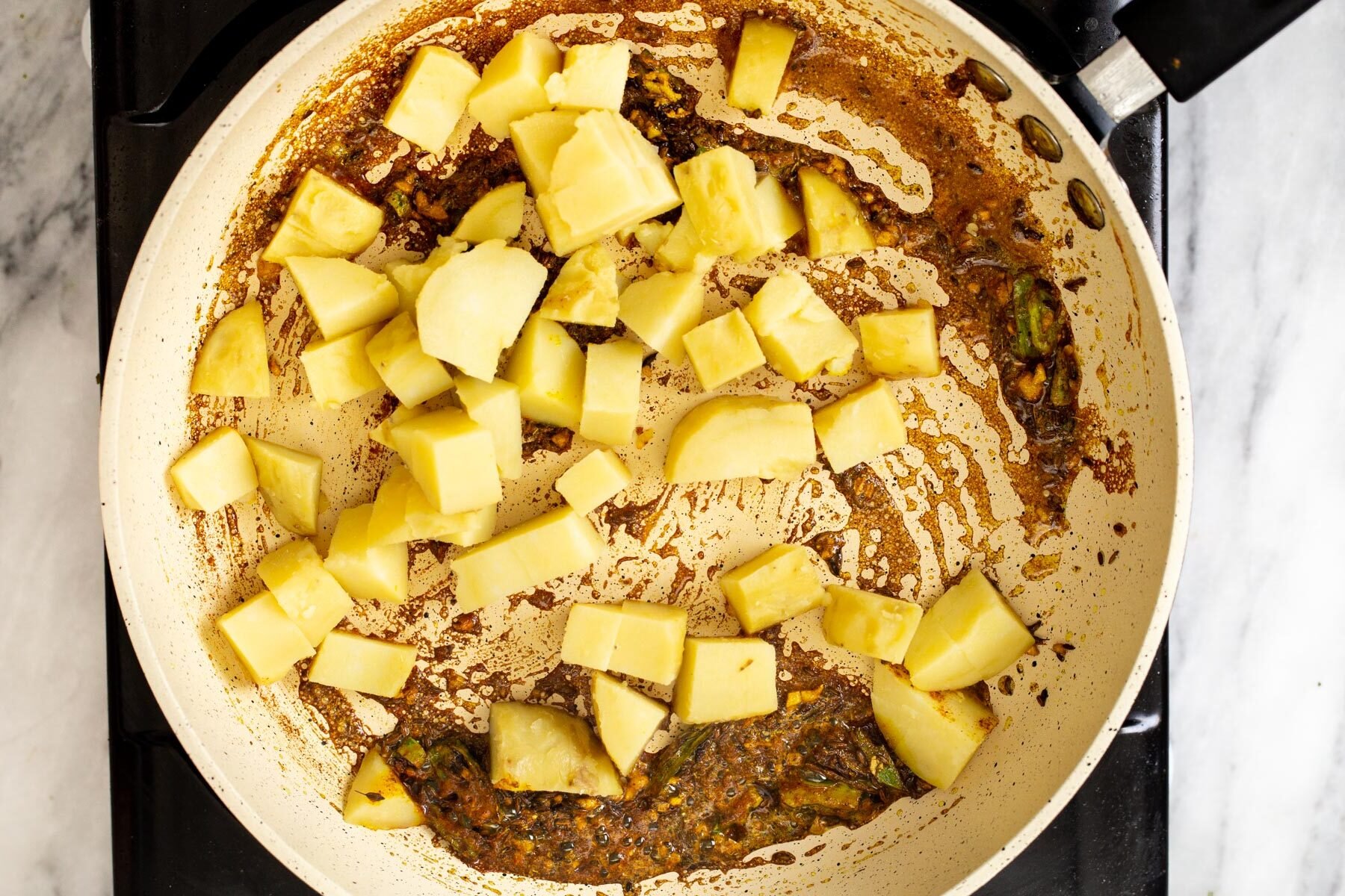 boiled potatoes being added to frying pan with spices