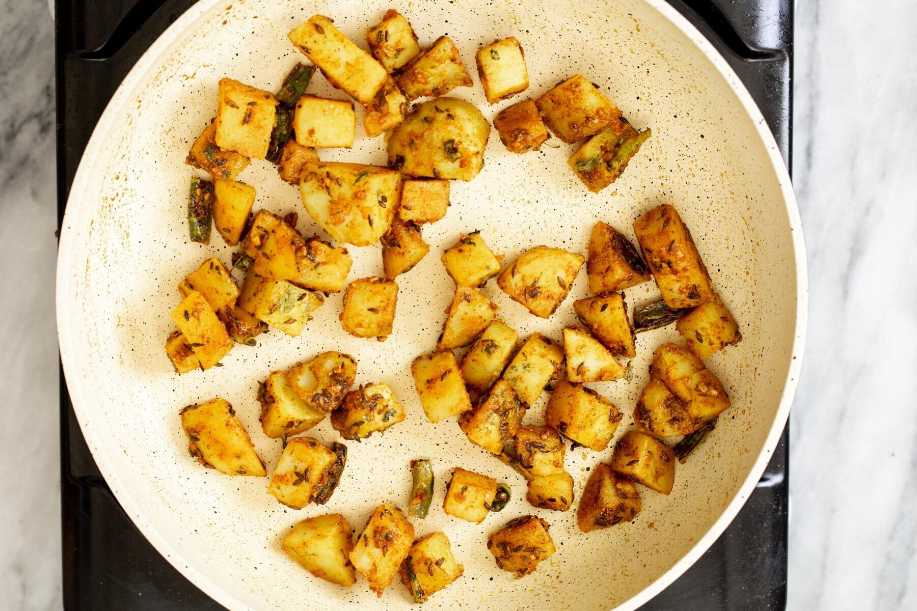 jeera potatoes in a white sauteeing pan