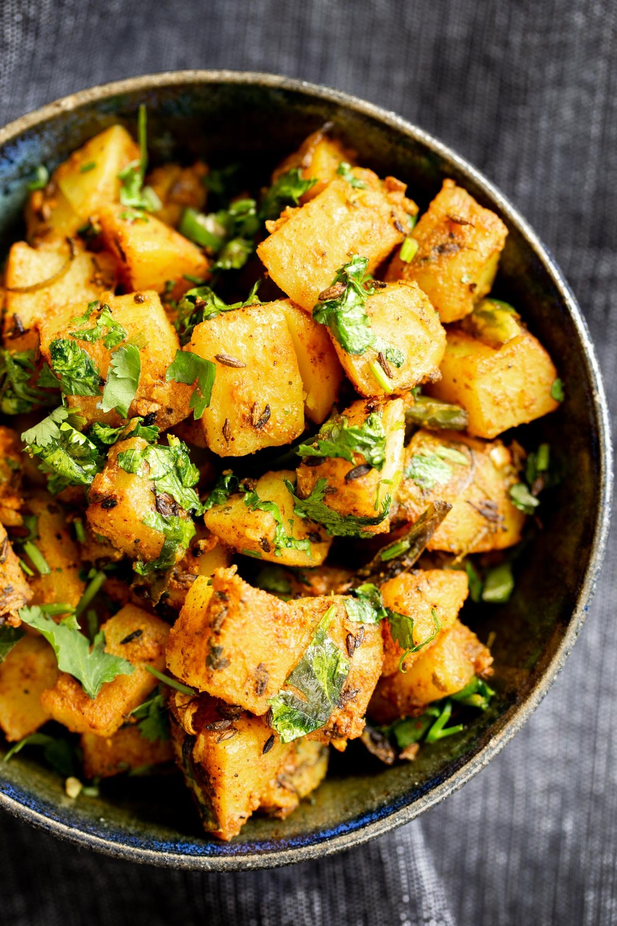 Indian cumin spiced potatoes sprinkled with cilantro served in a dark blue bowl