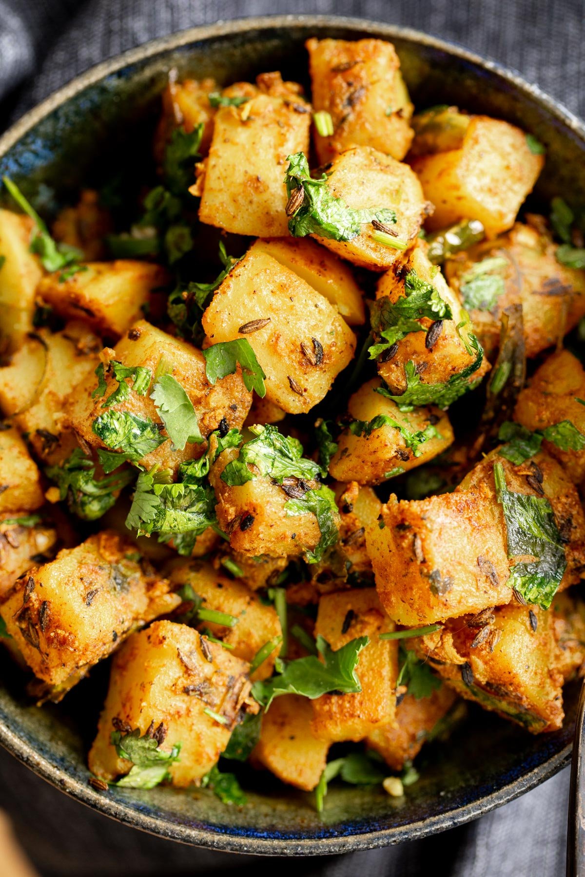 a bowl with cumin spiced jeera aloo potatoes sprinkled with fresh coriander