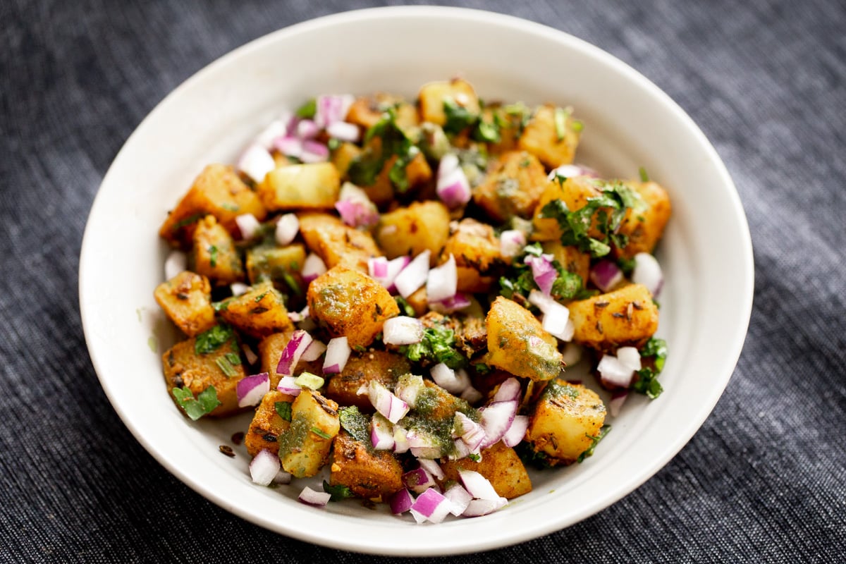 a small plate with jeera potatoes sprinkled with minced onions and cilantro