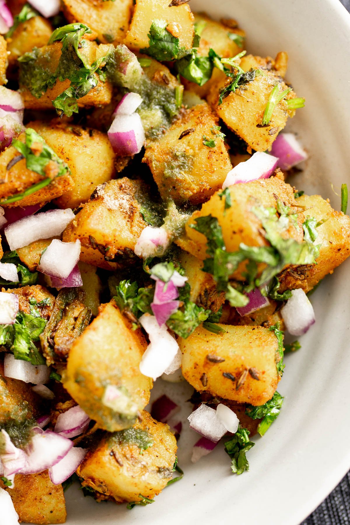 jeera aloo potatoes with fresh cilantro and chopped red onions in a white bowl
