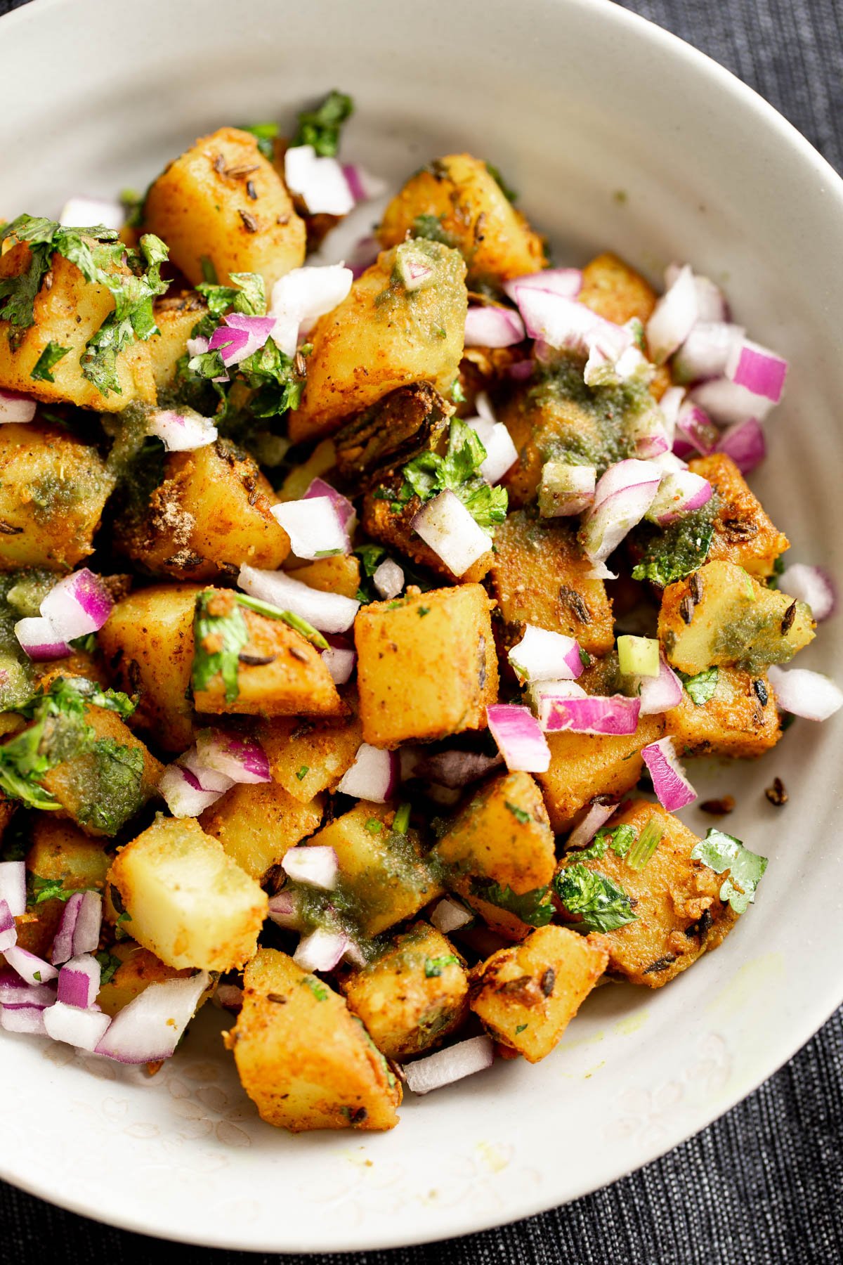 cumin spiced potatoes served in a white bowl sprinkled with coriander