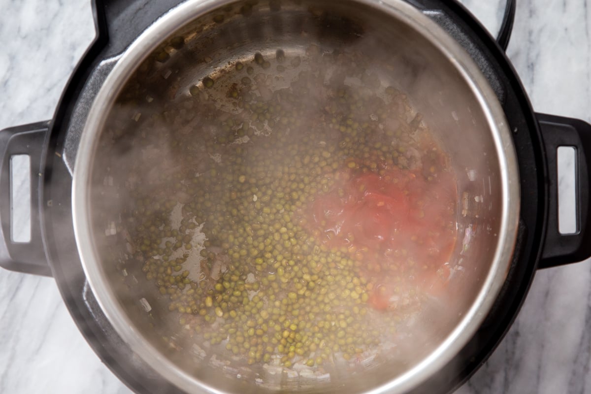 tomatoes and mung beans being added to sauteed onions to make dal