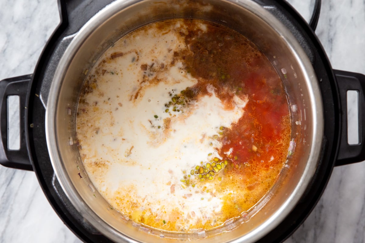 coconut milk being added to green mung beans, tomatoes and spices to make Instant pot dal