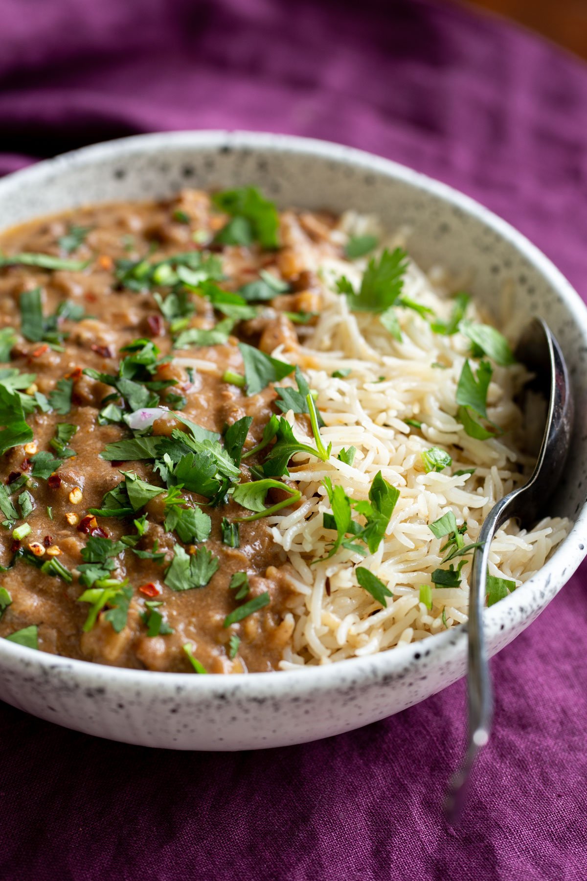 Indian mung bean curry with basmati rice served in a white bowl served with a spoon on the side