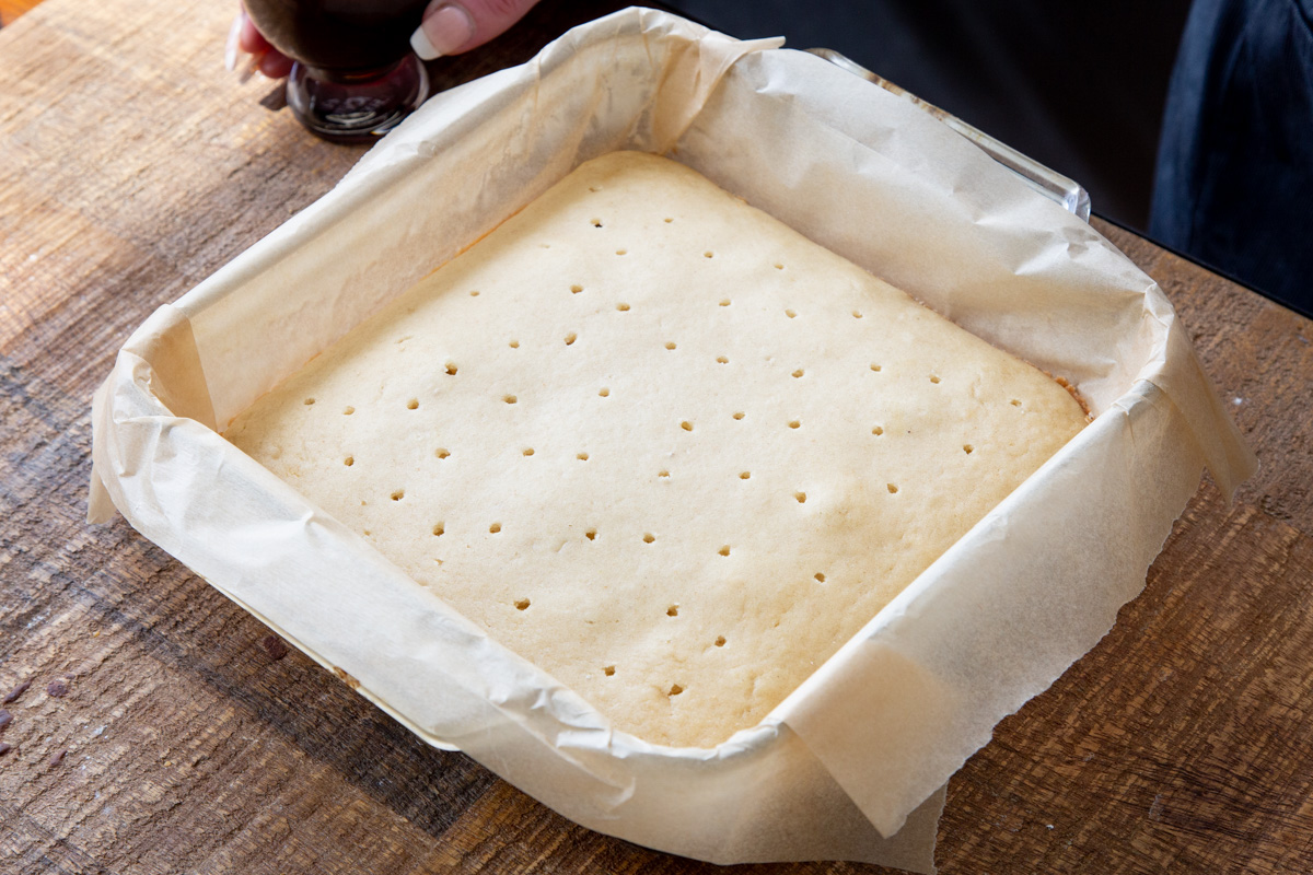 vegan sponge cake in a square pan being poked with holes