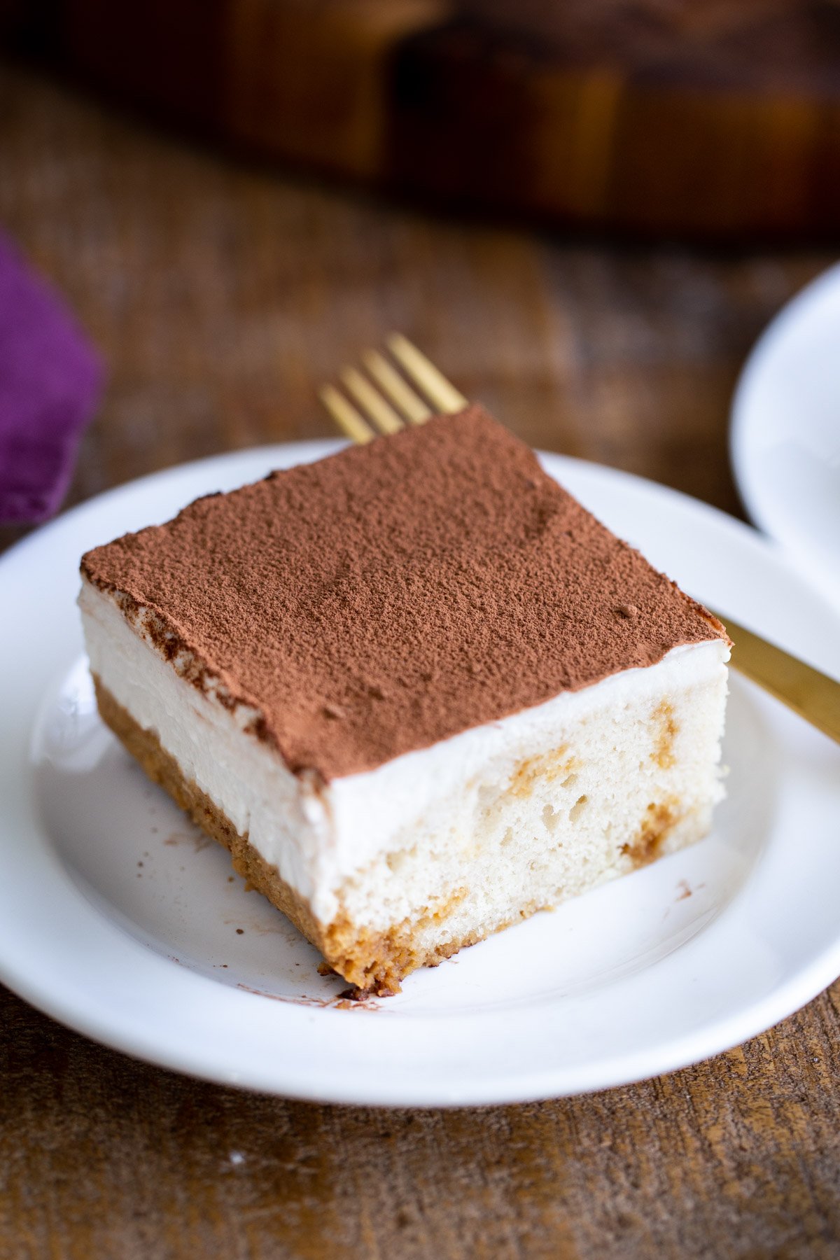 a slice of vegan tiramisu cake with mascarpone topping and dusted with cocoa on a white plate