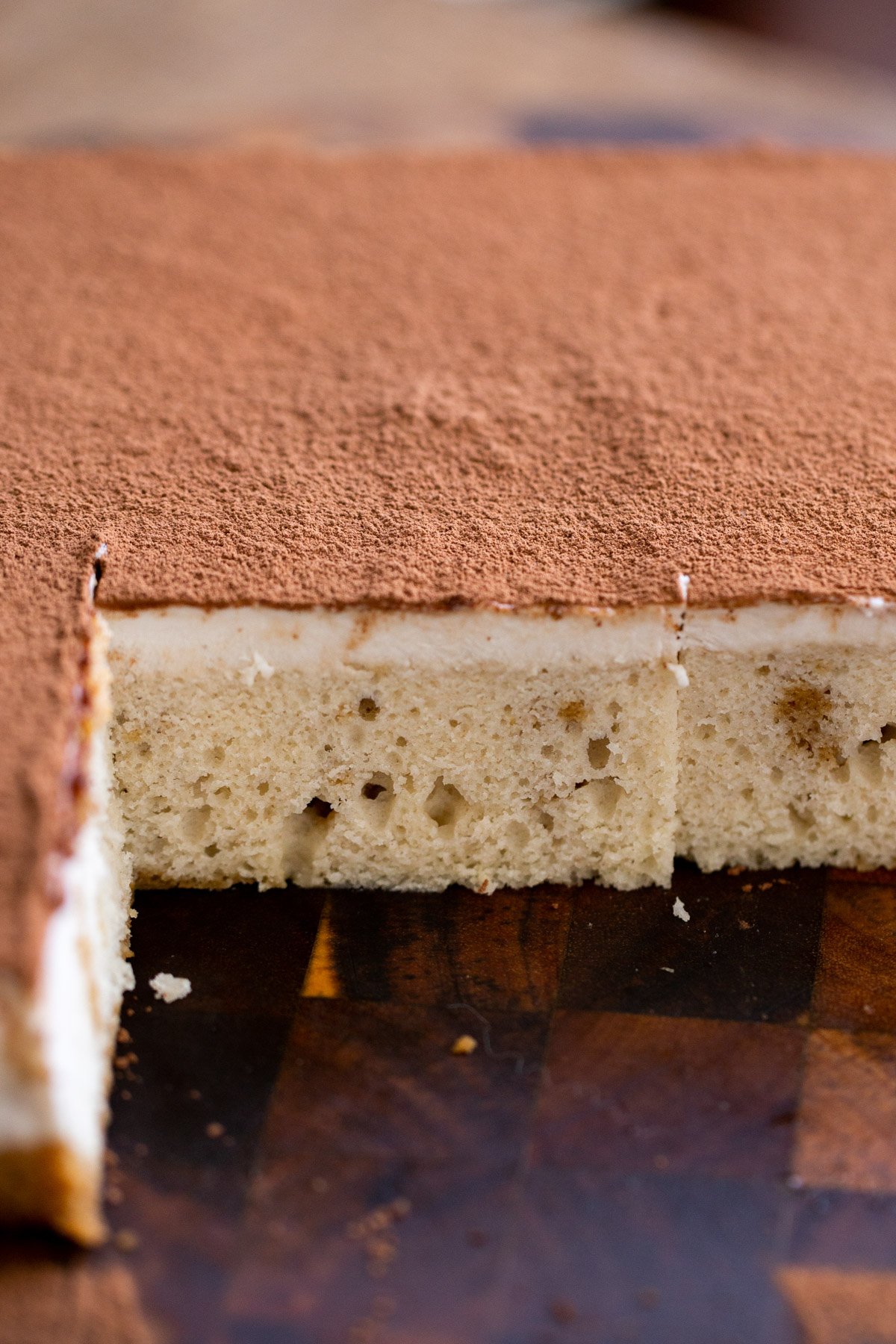 vegan tiramisu sheet cake on a wooden board dusted with cocoa powder