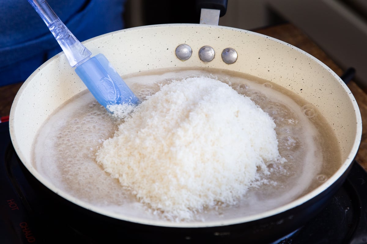 shredded coconut being added to a sauteeing pan with coconut milk