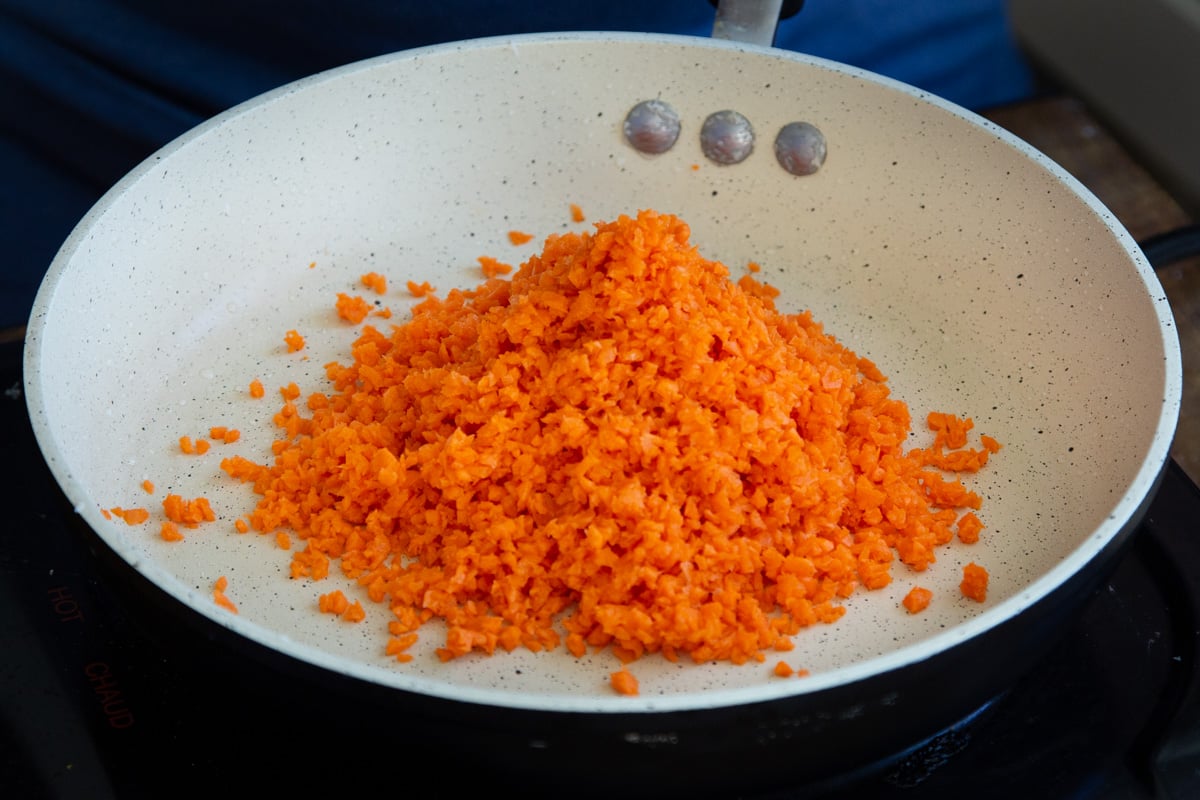 shredded carrots being added to sauteeing pan