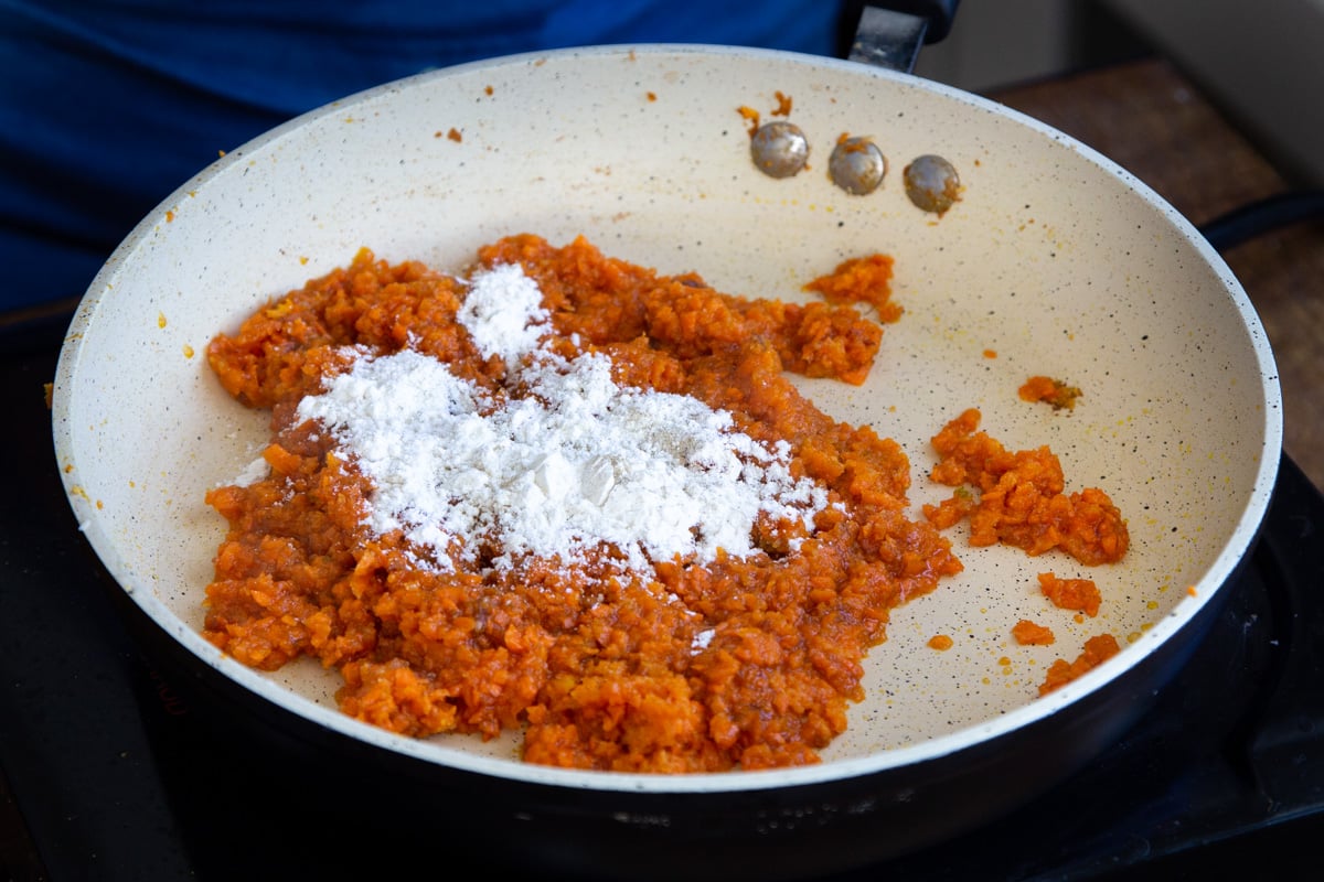 flour being added to shredded carrots in a frying pan