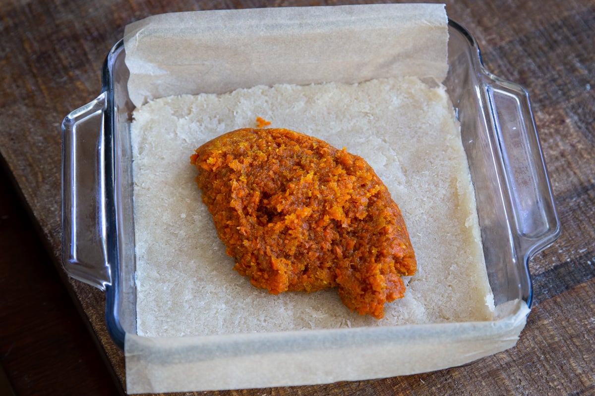 carrot halwa layer being spread over coconut burfi layer in a square glass pan