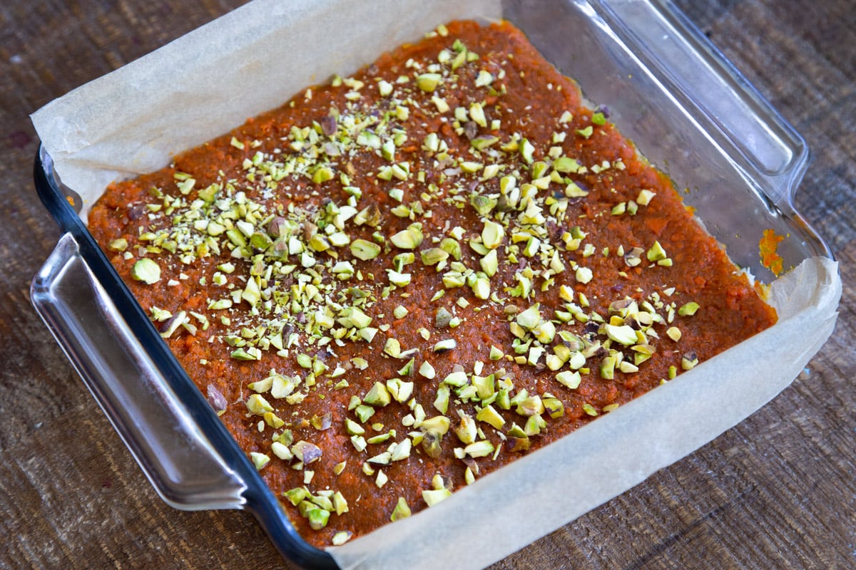 carrot halwa coconut burfi bars topped with chopped pistachios in a glass dish