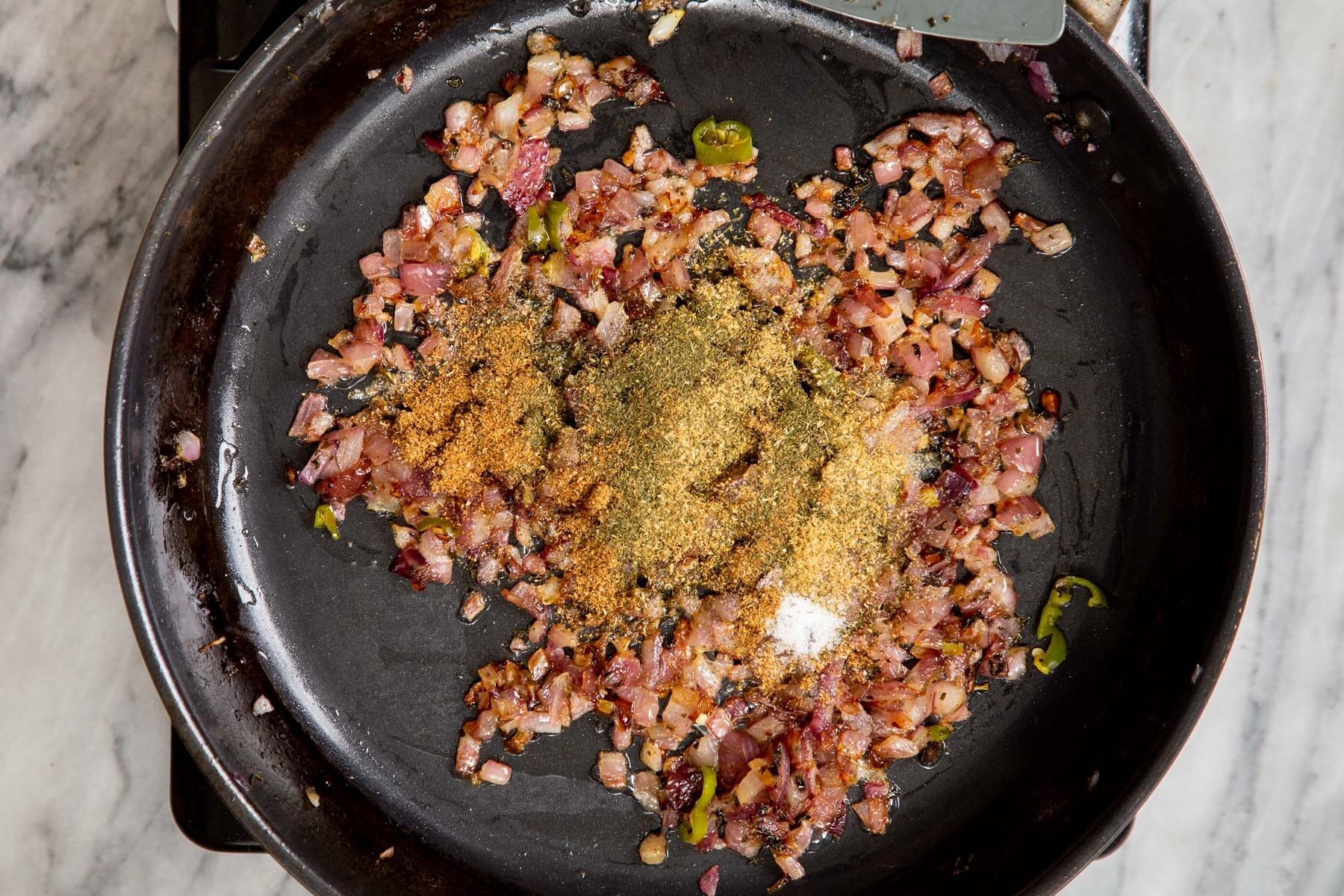 ground spices and minced onions in a black frying pan