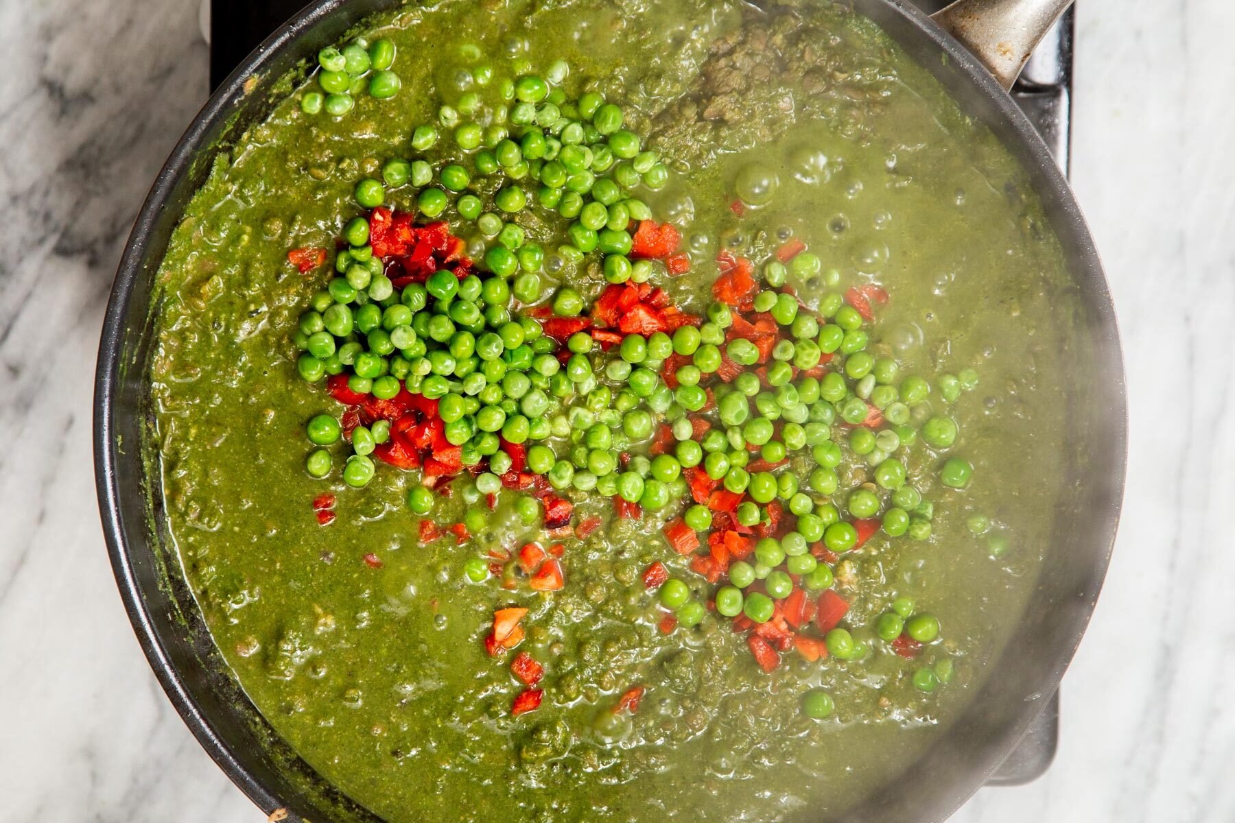 peas and red pepper being added to vegan keema in a black skillet