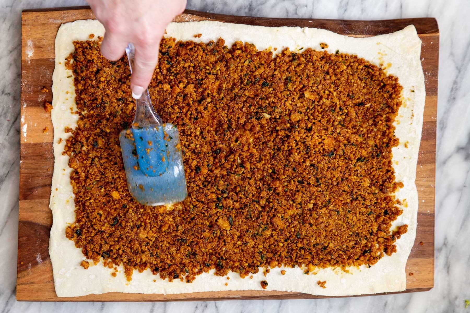 vegan lentil filling being spread out on a sheet of puff pastry