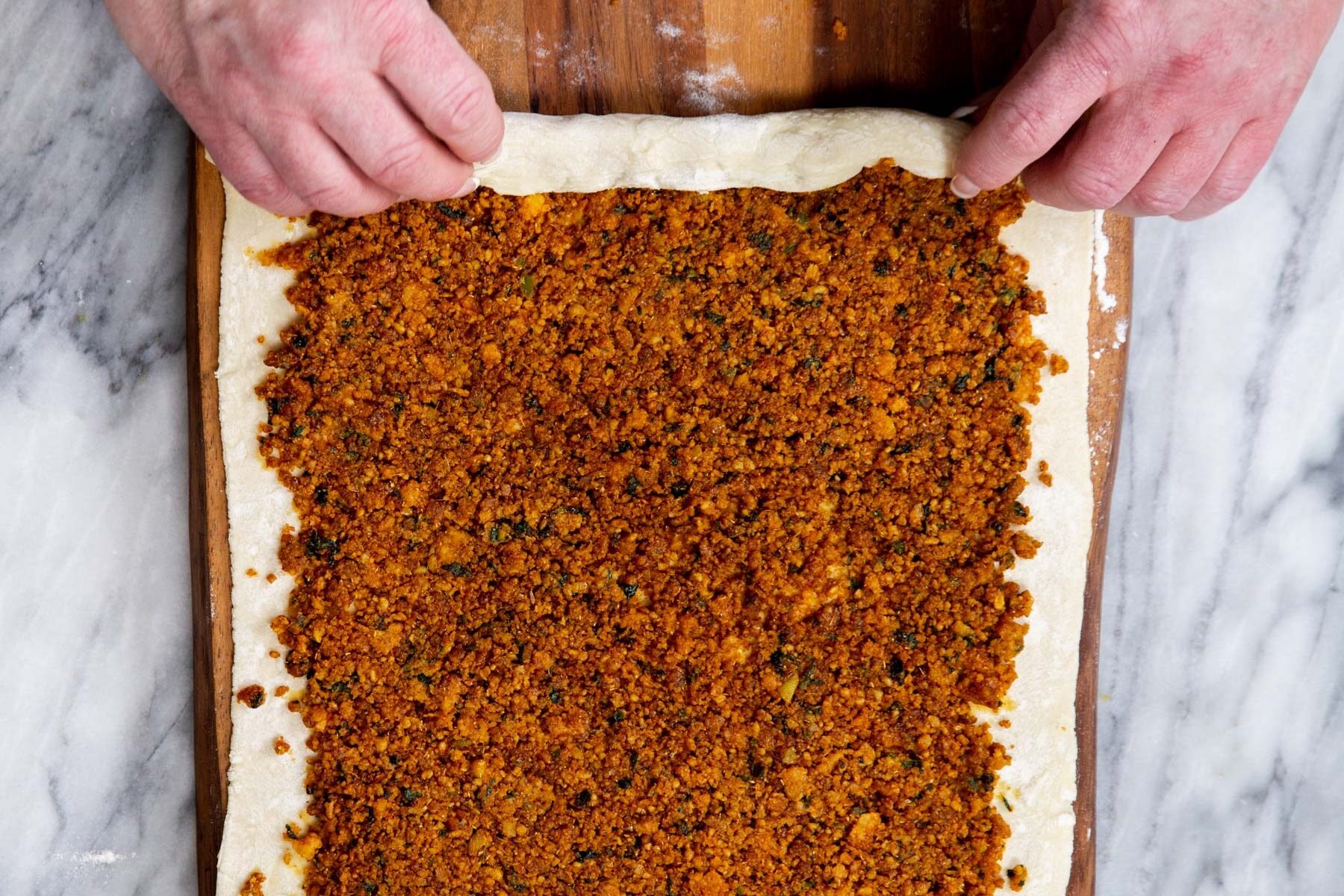 a sheet of puff pastry with lentil filling being rolled up to make pinwheels