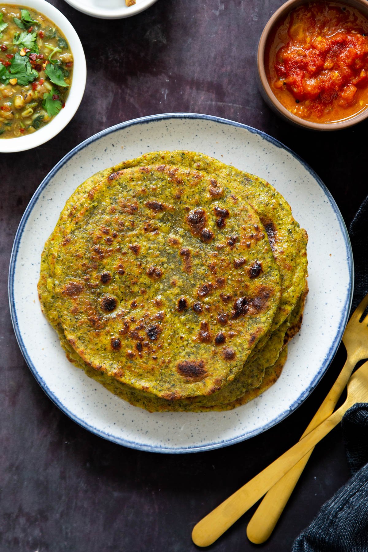 three masala parathas with small dishes of chutney and golden cutlery