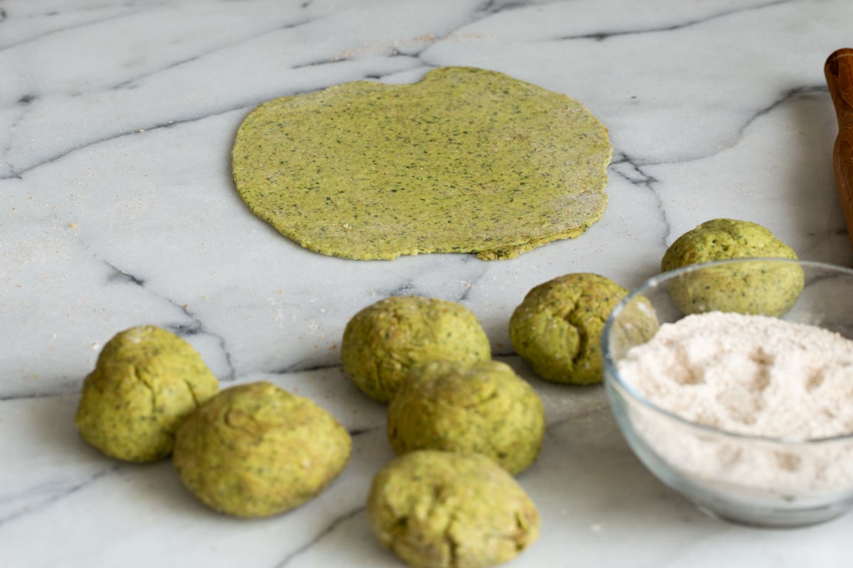 small rolled balls of paratha dough on a marble countertop with a small dish of flour on the side