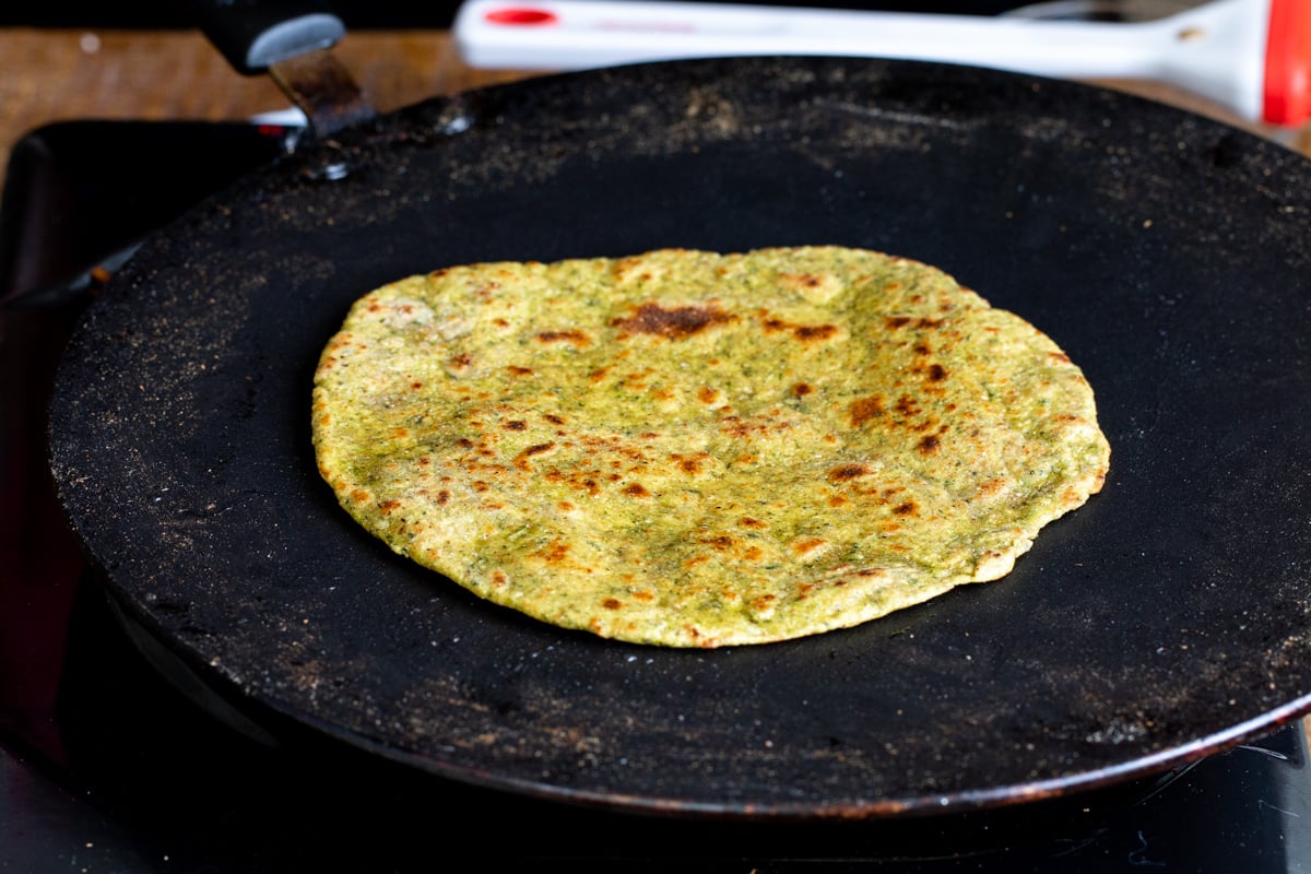 freshly toasted masala paratha in a black flat skillet