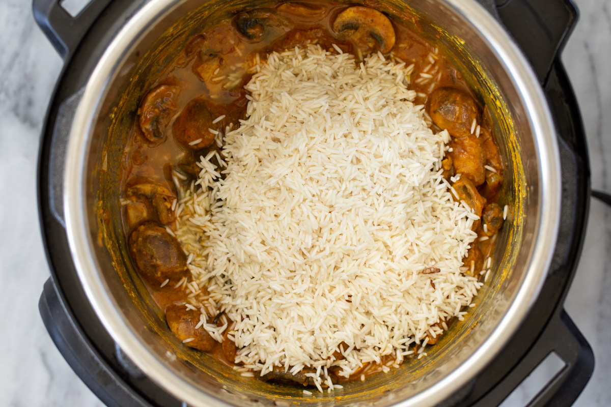 drained rice being added to mushrooms in spicy gravy in an Instant Pot