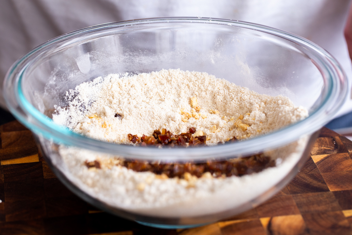 chopped dates and nuts being added to dry cookie ingredients in glass bowl