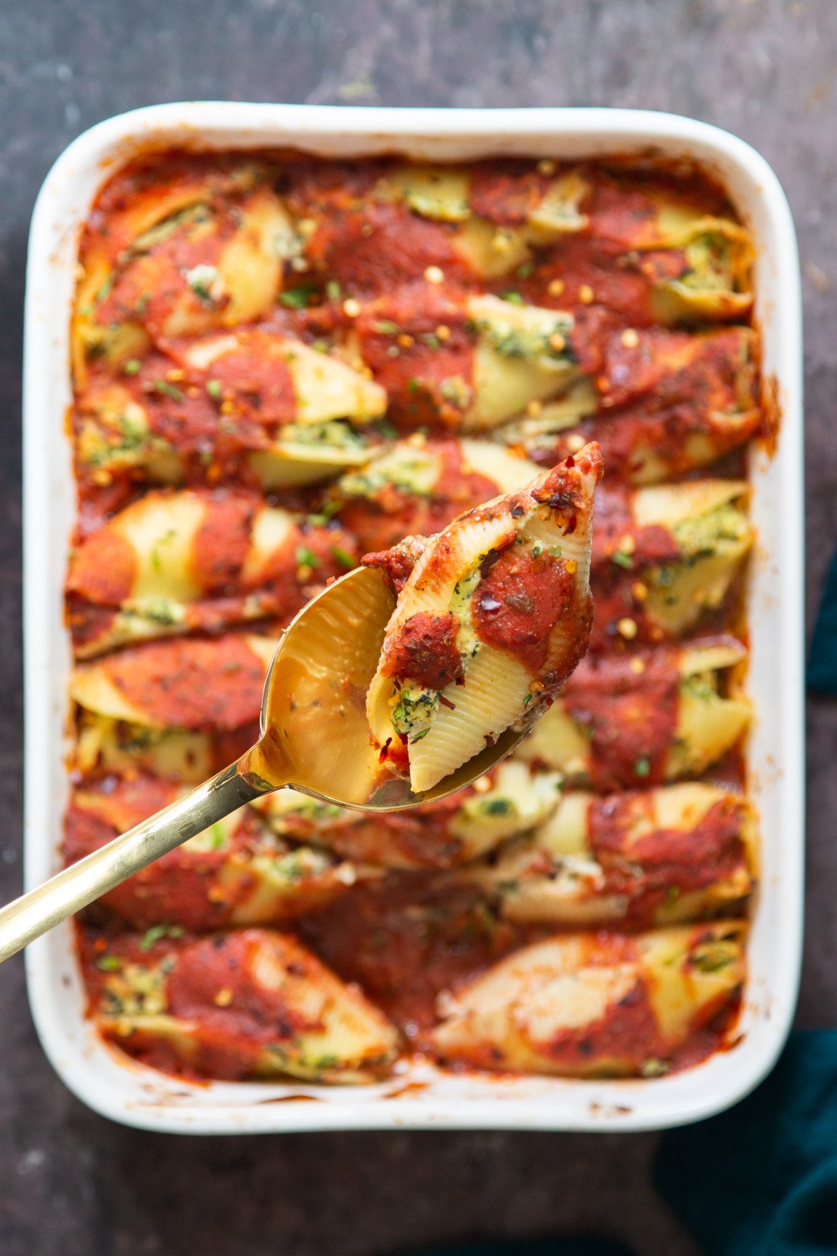 a spoon with a vegan stuffed shell being held over a casserole dish