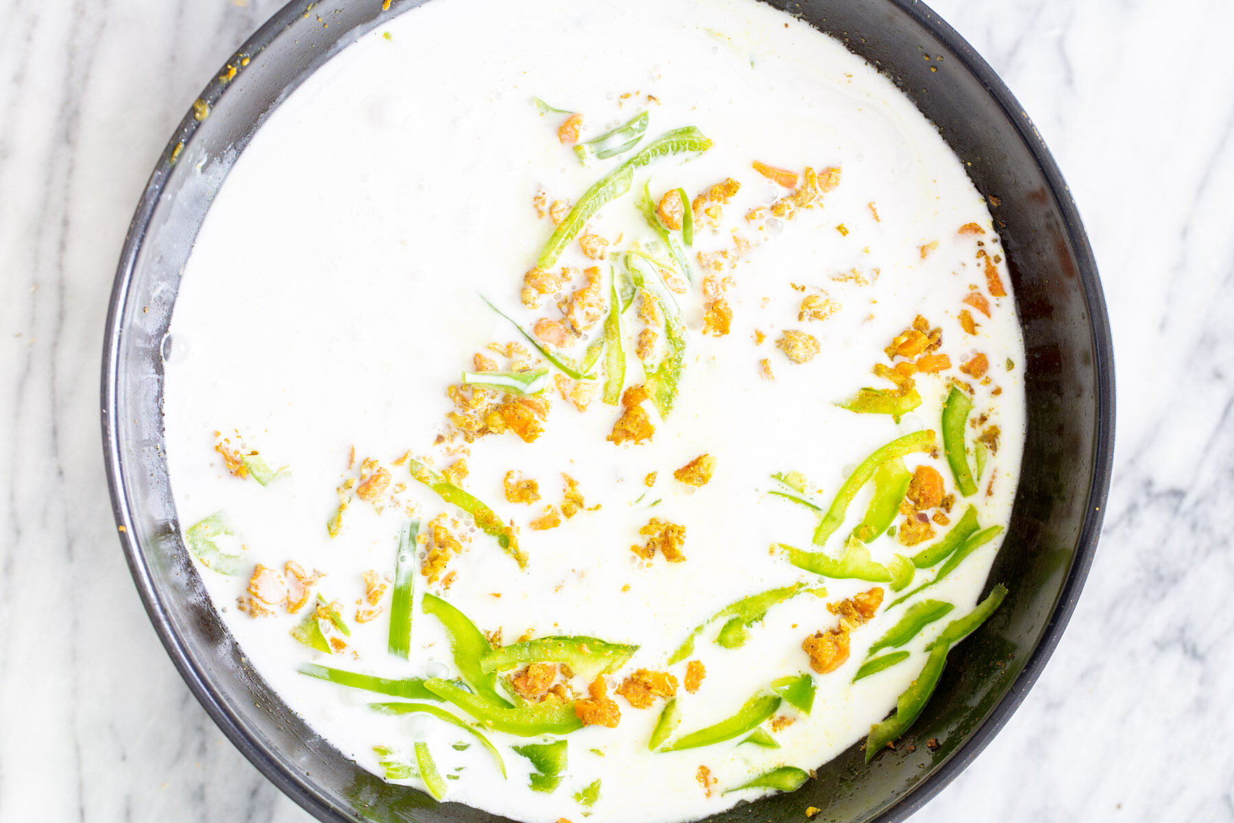 coconut milk being added to spiced veggie mix in a black skillet