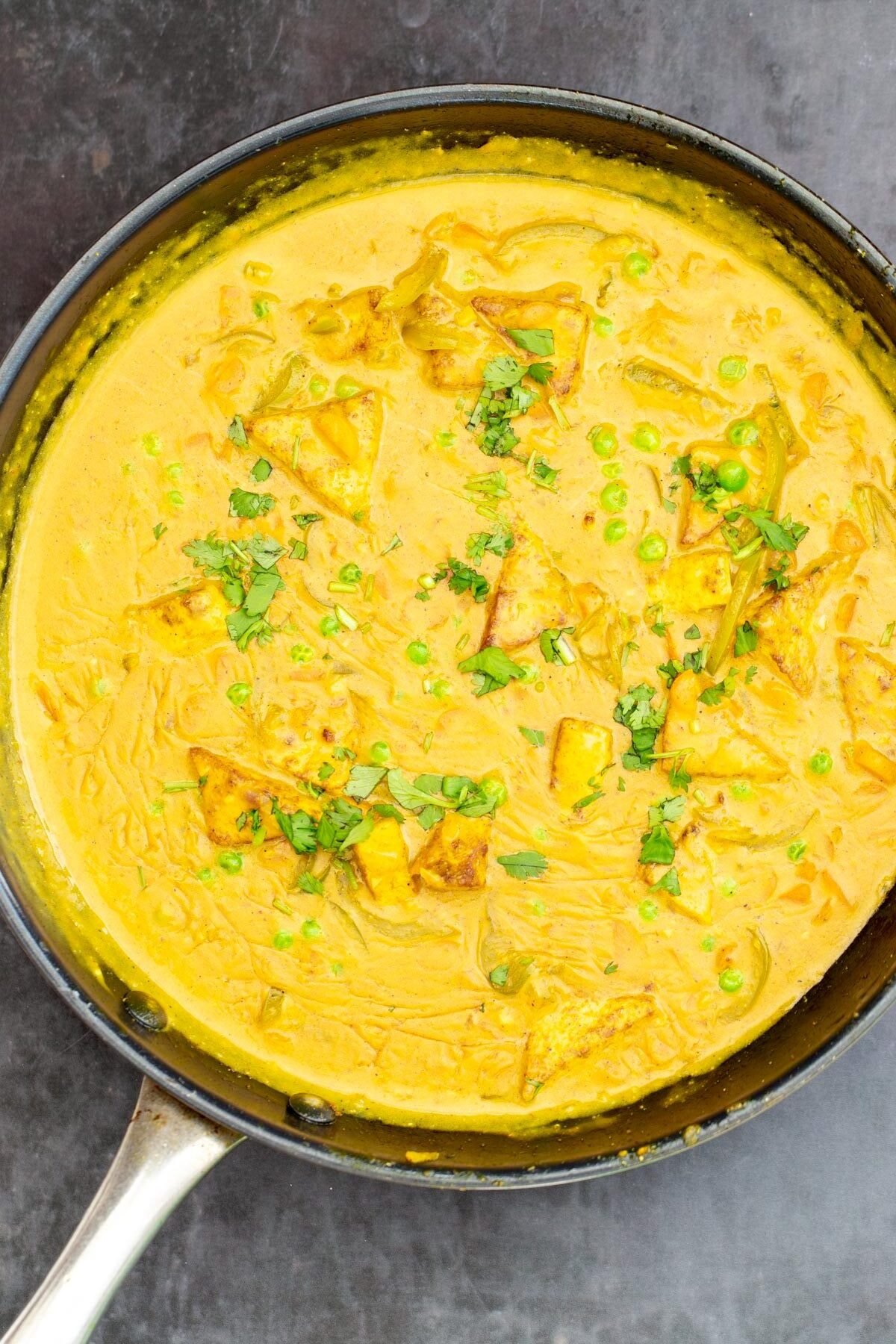 creamy Malaysian tofu coconut milk curry in a black skillet sprinkled with cilantro