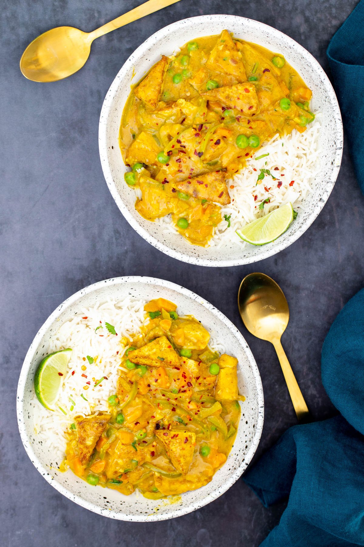 two bowls with rice and malaysian coconut tofu curry served with two golden spoons