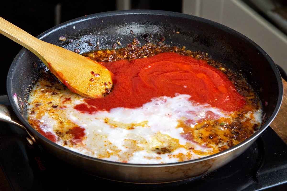 coconut milk and tomato paste simmering in a pan along with spices to make gravy