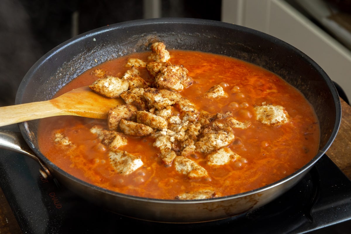 marinated baked tofu chunks being added to tomato gravy in a skillet