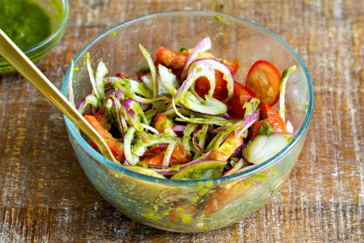 onion, tomatoes and cilantro mint chutney being mixed in a glass bowl