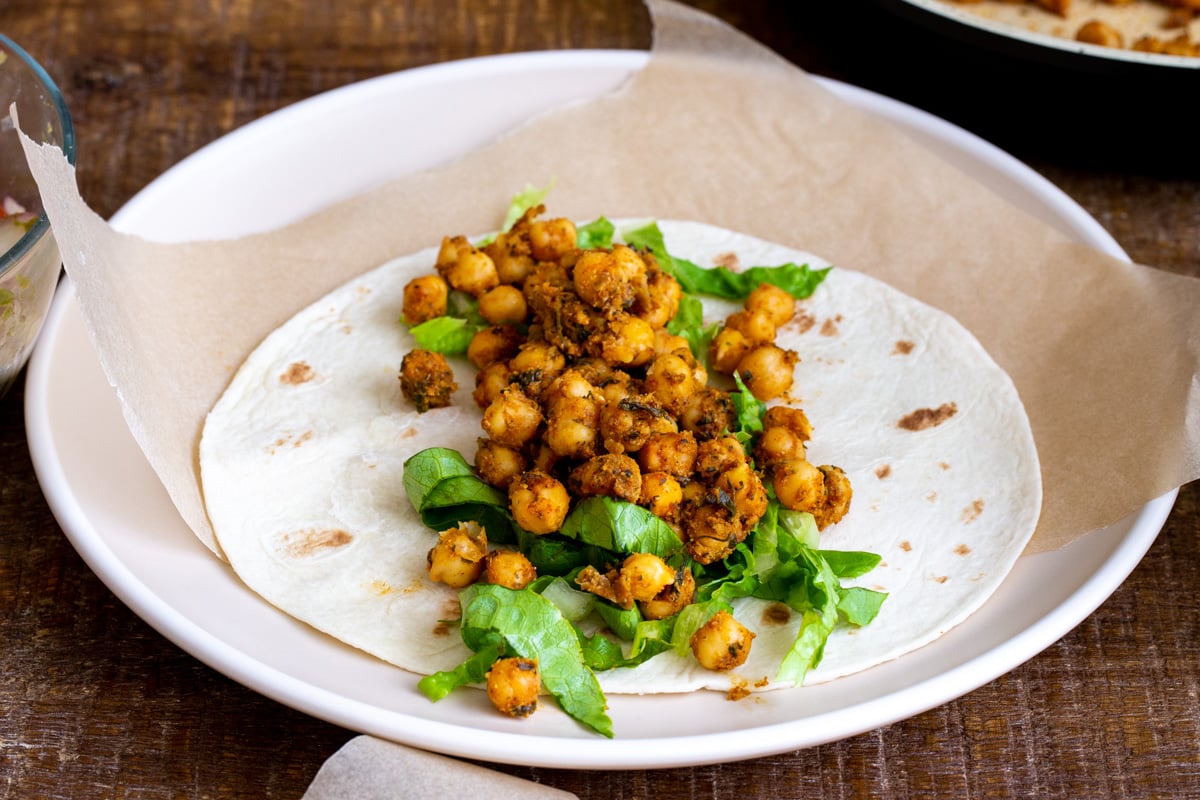 spiced chickpea and chopped lettuce being added to a wheat tortilla to make a wrap