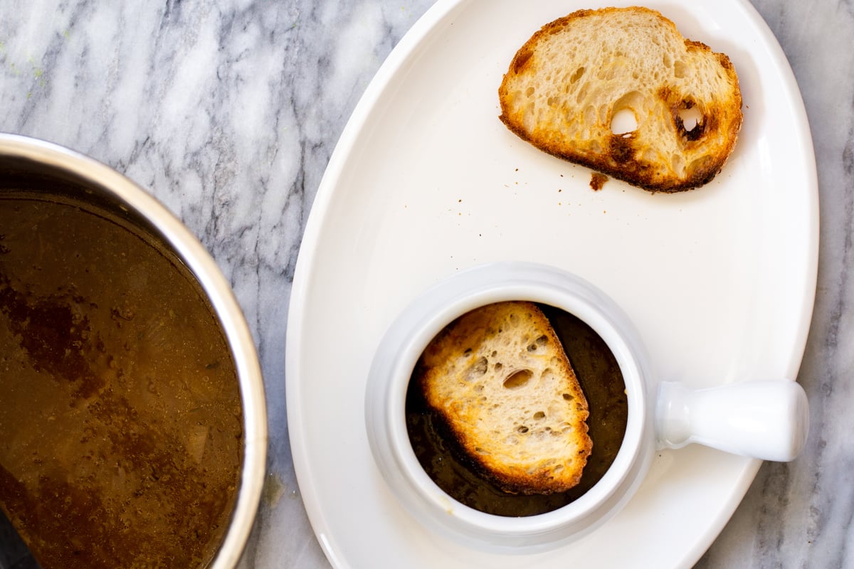 vegan french onion soup being topped with a slice of sourdough bread
